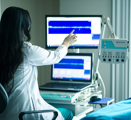 Doctor pointing at a patient monitor beside a hospital bed 