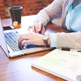 Woman typing on a laptop at a wooden table with a mug of tea beside here